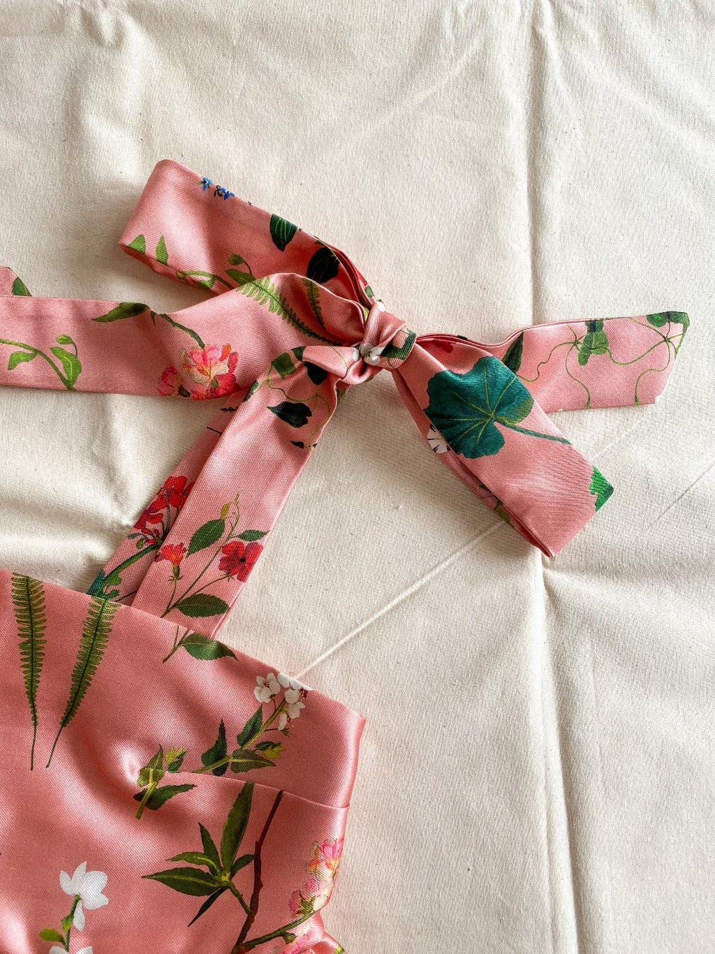 Close-up of the Meadow top, a cropped top made from a pink deadstock silk/cotton blend in a beautiful floral print.  The top is sleeveless and ties into bows at the shoulders.