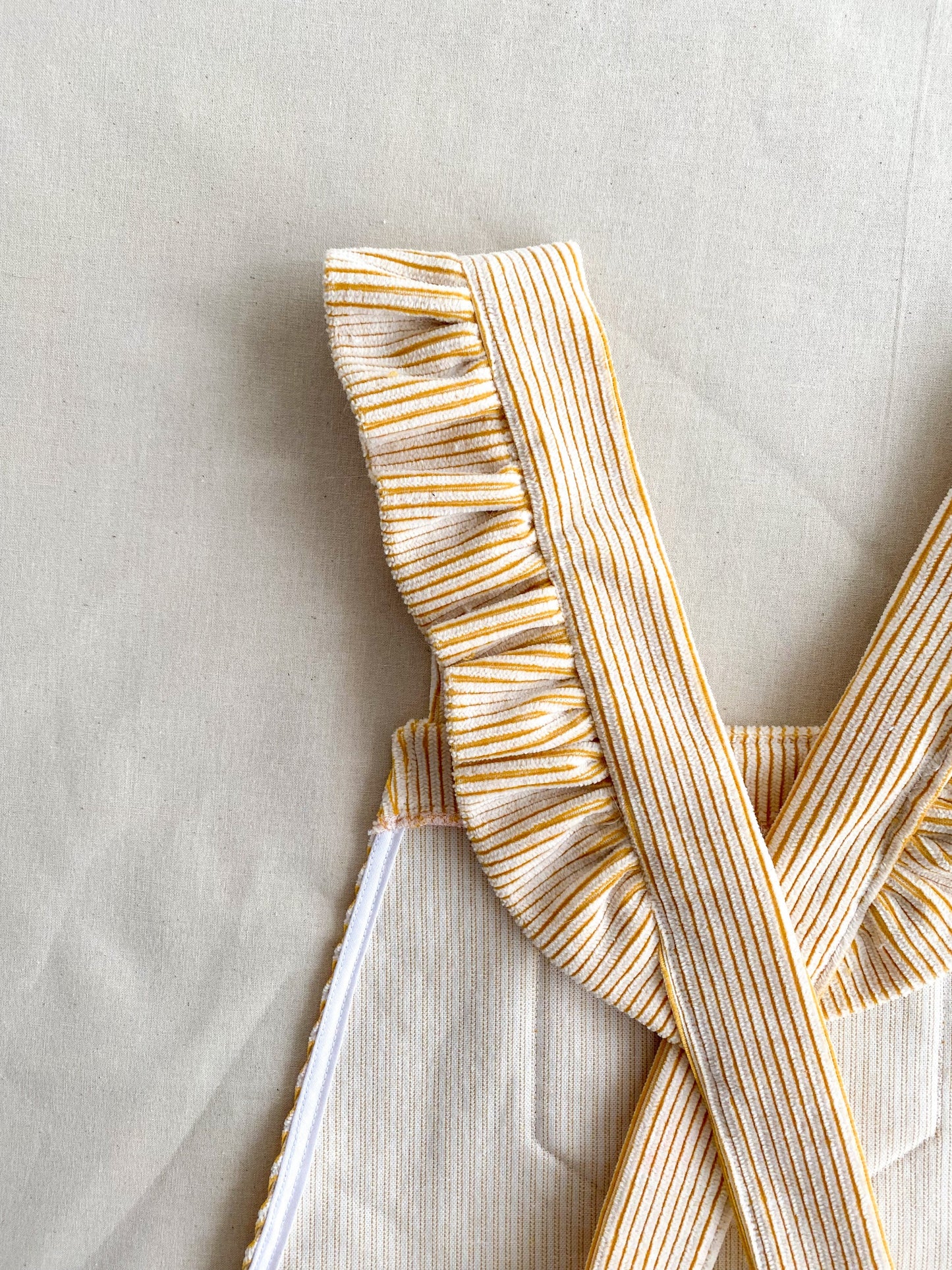 Close up picture of the Billie pinafore, a short length dungaree dress made from yellow and white deadstock corduroy. The picture focuses on the ruffles on the back of the shoulder straps.