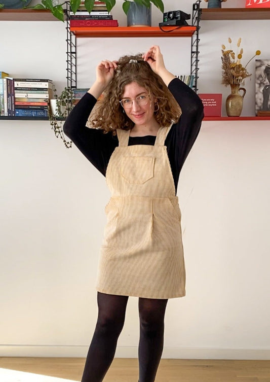 Picture of Leen, a twenty something white woman, posing in the Billie pinafore and smiling.
