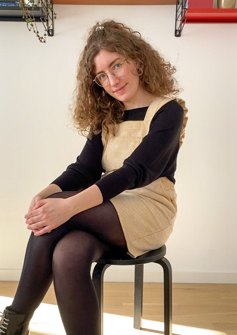 Picture of Leen posing in the Billie pinafore and smiling while sitting down.