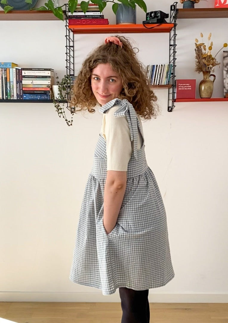 Side profile picture of Leen, a twenty something white woman, posing in the Alice dress, smiling and with her hands in the pockets of the dress.