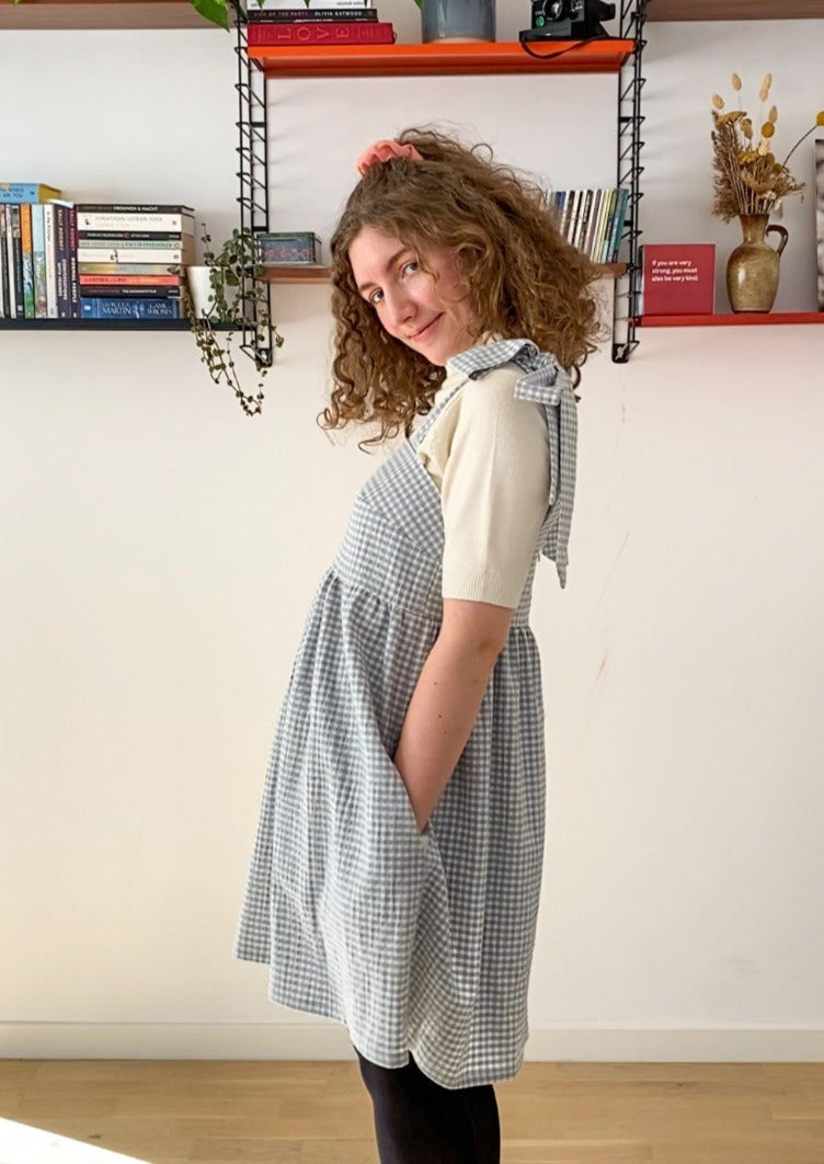 Side profile picture of Leen posing in the Alice dress, smiling and with her hands in the pockets of the dress.