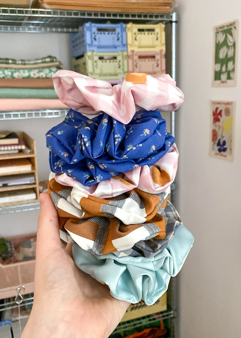 Stack of colorful scrunchies held in front of a shelf with various items.