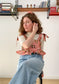 Picture of Leen, a twenty something white woman, posing in the Meadow top while sitting down.