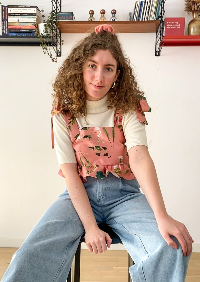 Picture of Leen, a twenty something white woman, posing in the Meadow top and smiling while sitting down.