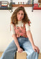 Picture of Leen, a twenty something white woman, posing in the Meadow top and smiling while sitting down.